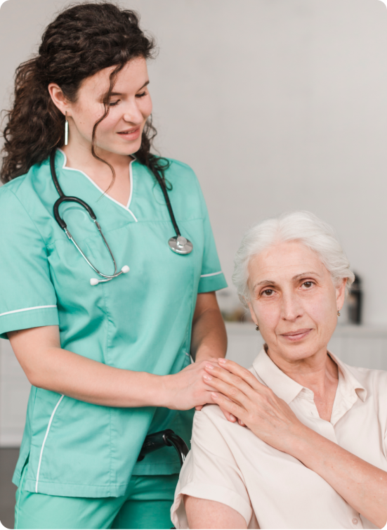 praestivo_ A nurse in green scrubs with a stethoscope smiles and gently places her hands on the shoulder of an older woman with gray hair, who is sitting and looking at the camera.